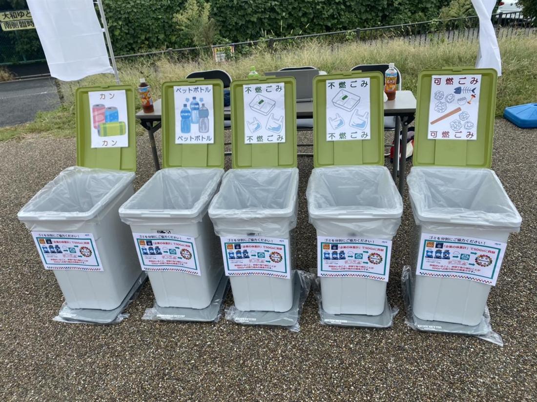 屋外のイベント会場に並べられた分別用のごみ箱。ペットボトル、可燃ごみ、不燃ごみなどの表示が付いている。