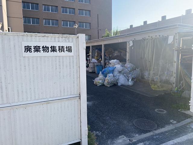 屋根付きの廃棄物集積場。金属かごにごみ袋が集積されている。