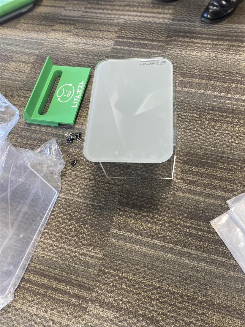 企業の体重計®の計量器本体を間近から見た様子。白い薄型のプレート型端末が透明な台の上に置かれている。